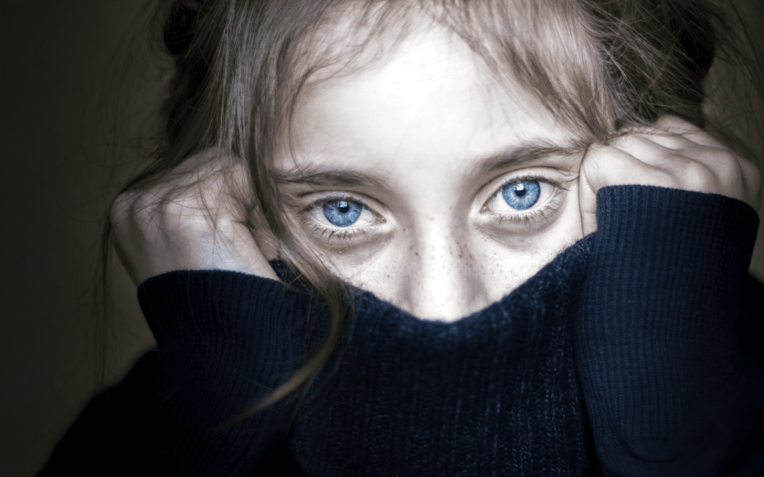 Girl with blue eyes pulling a black sweater over her face in a show of fear