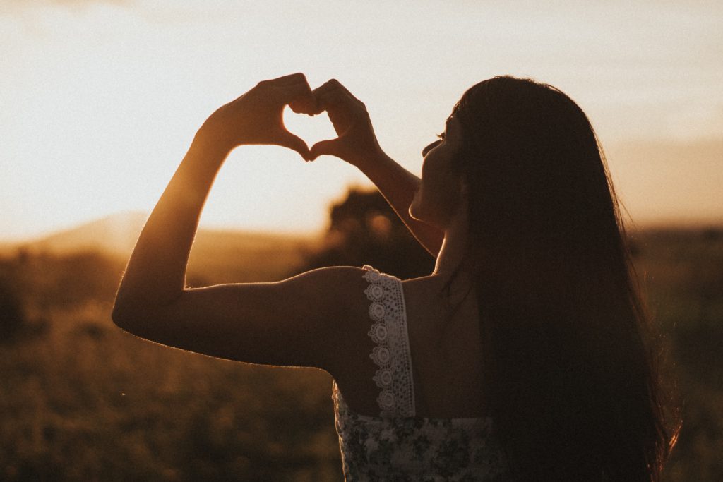 Picture of a woman displaying a heart sign at twilight representing self-compassion