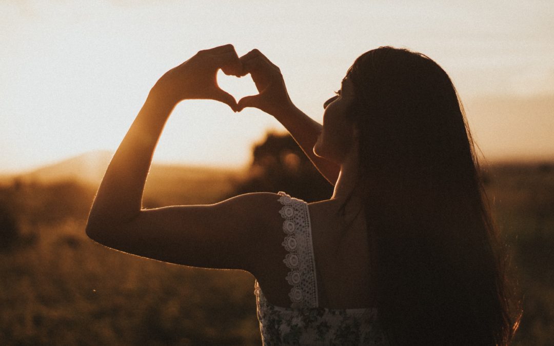 Picture of a woman displaying a heart sign at twilight representing self-compassion