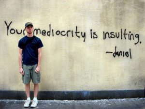 Picture of a man along a graffiti that says being mediocre is insulting for John R. Miles blog