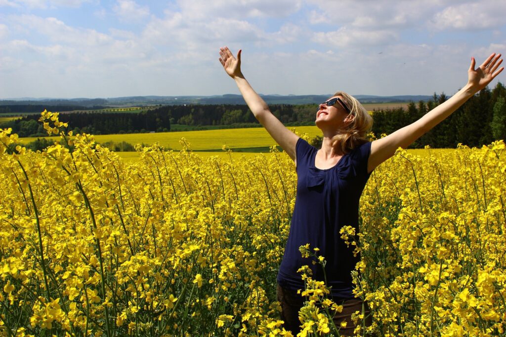 Woman showing the regenerative power of gratitude as she lifts her hands to the sky in a field of flowers