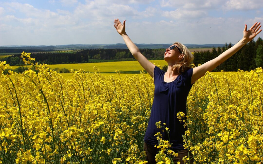 Woman showing the regenerative power of gratitude as she lifts her hands to the sky in a field of flowers